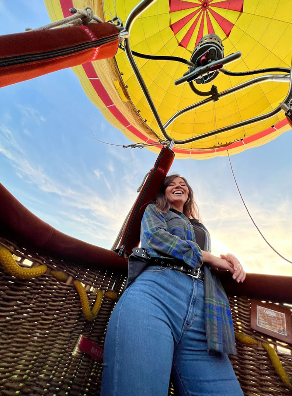Donna sorridente a bordo di una mongolfiera gialla con vista del cielo al tramonto